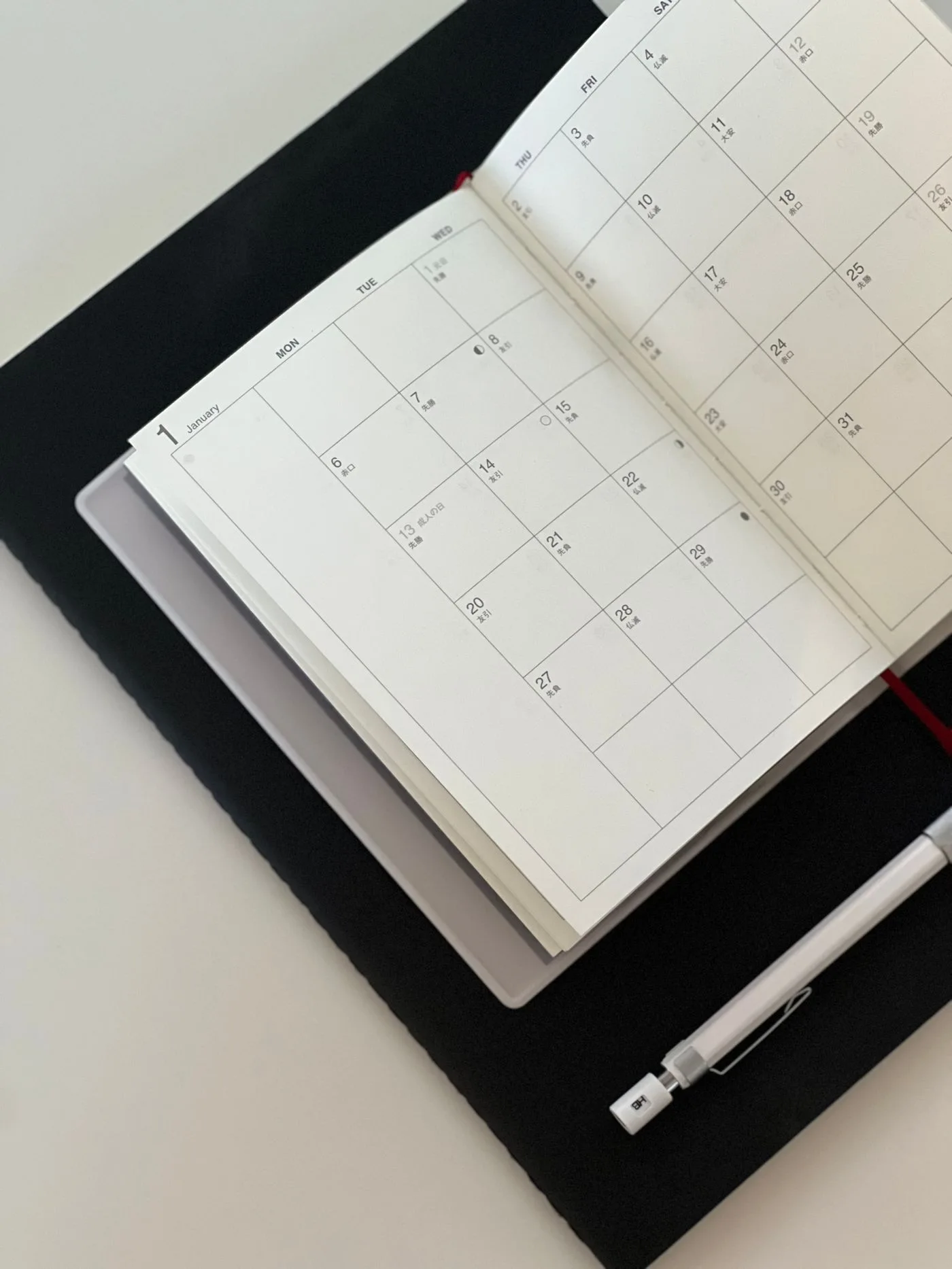 Open planner with calendar on desk, accompanied by pen and tablet.