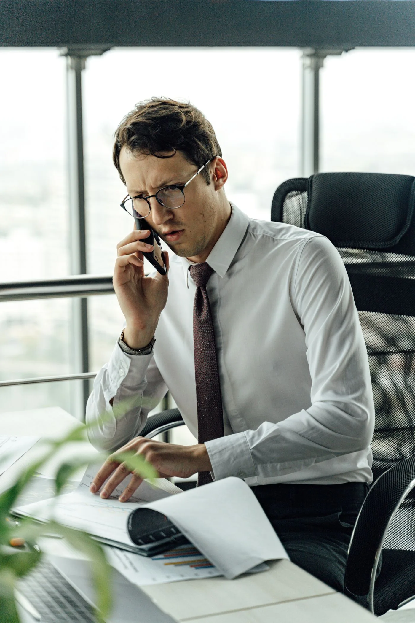 A businessman engaged in a phone call while reviewing documents in a modern office.