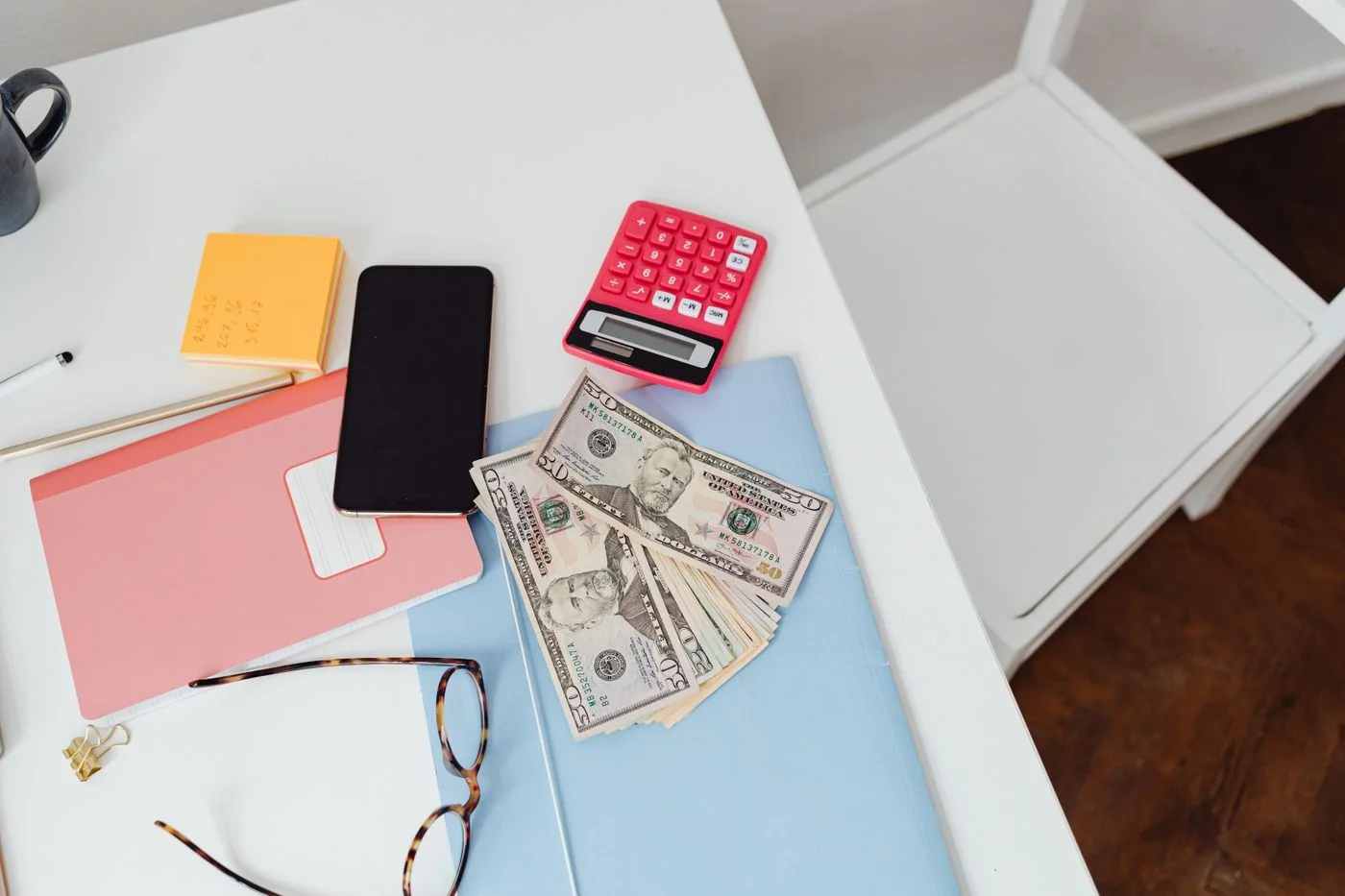 Overhead view of office desk with calculator, money, and glasses, depicting finance and budgeting.