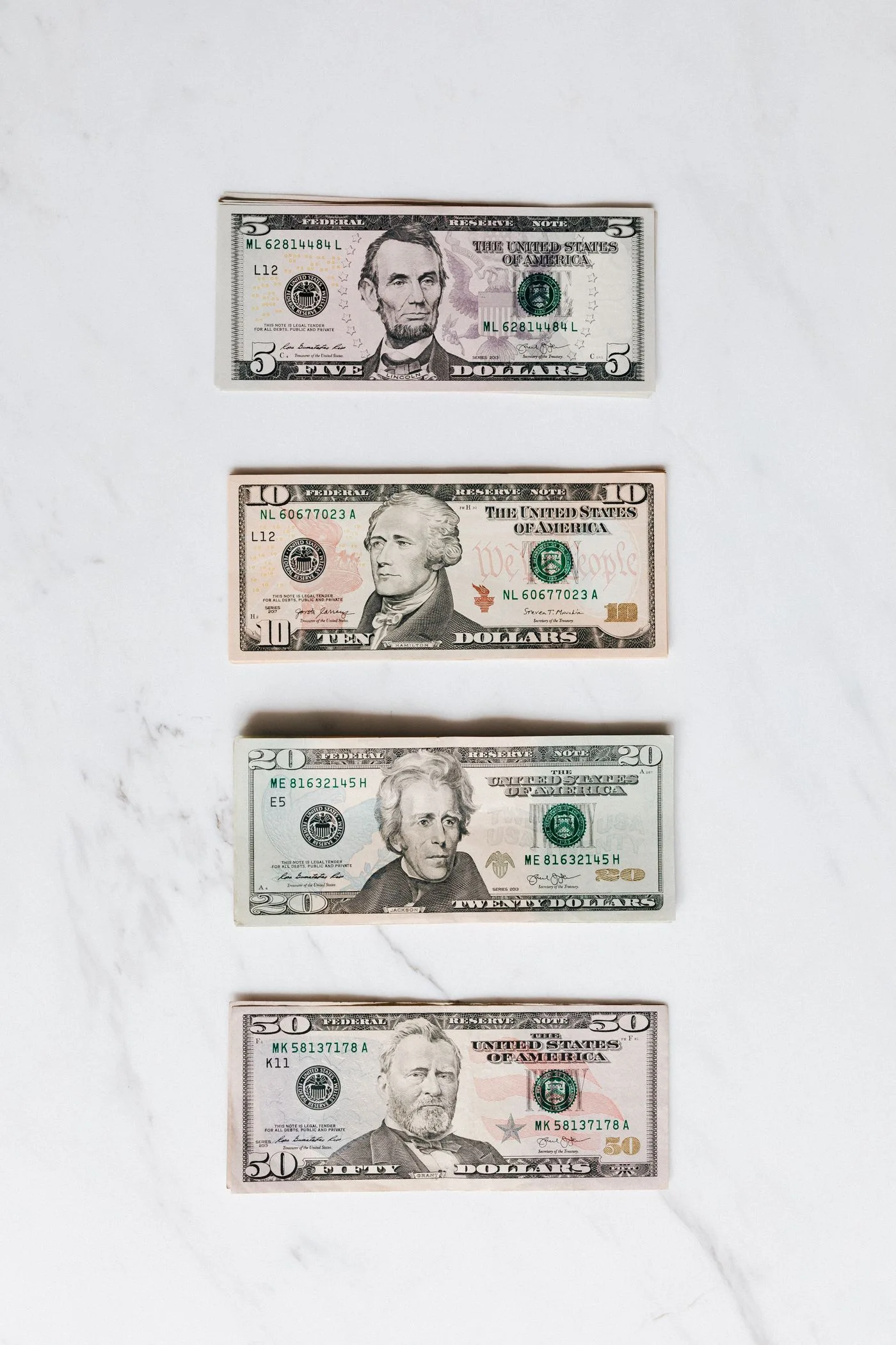 Top view of American dollars placed in order of increasing of banknotes nominal par on white marble surface