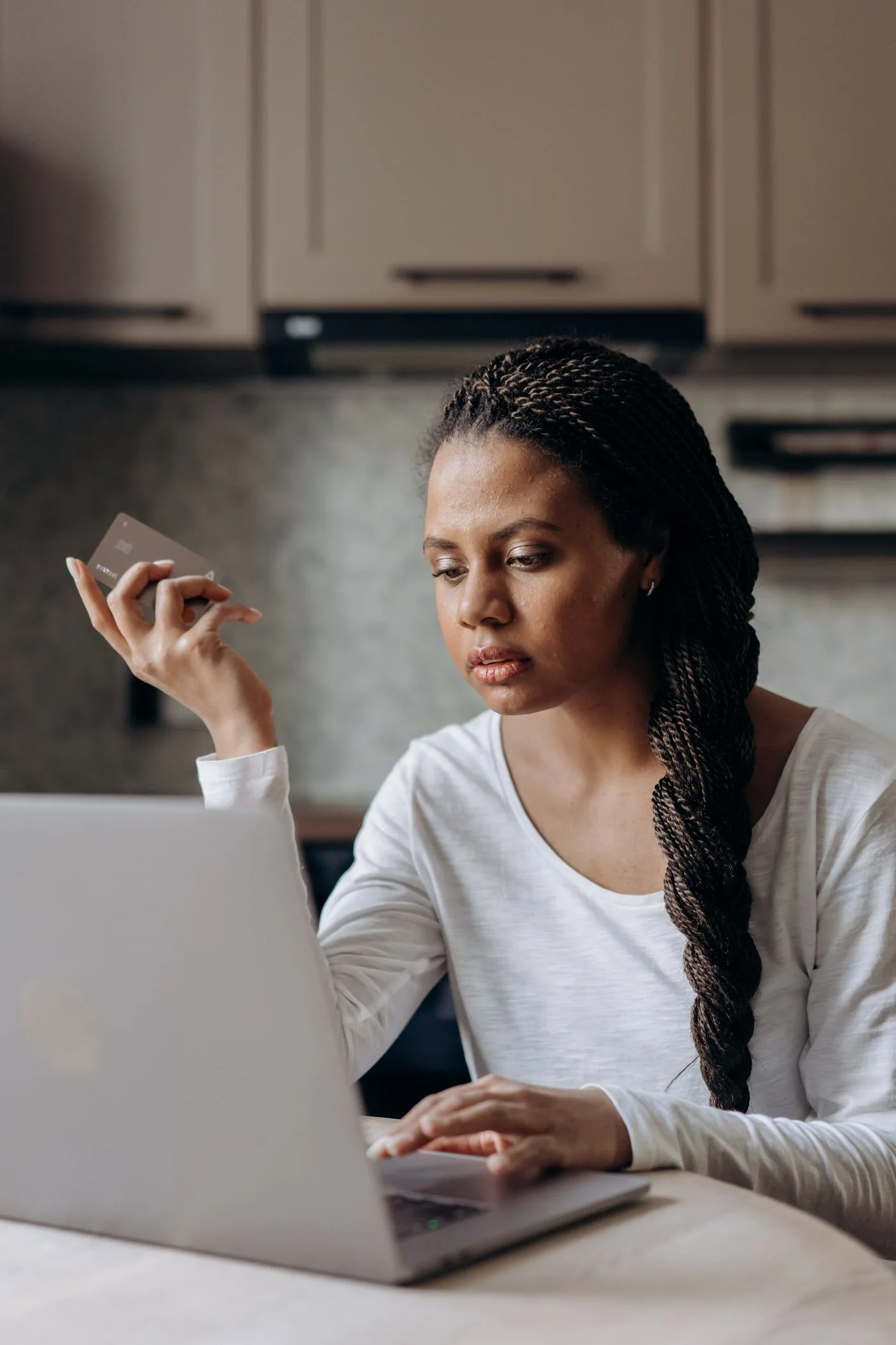 Image: Free Woman with braided hair uses laptop and credit card for online banking in a modern home setting.