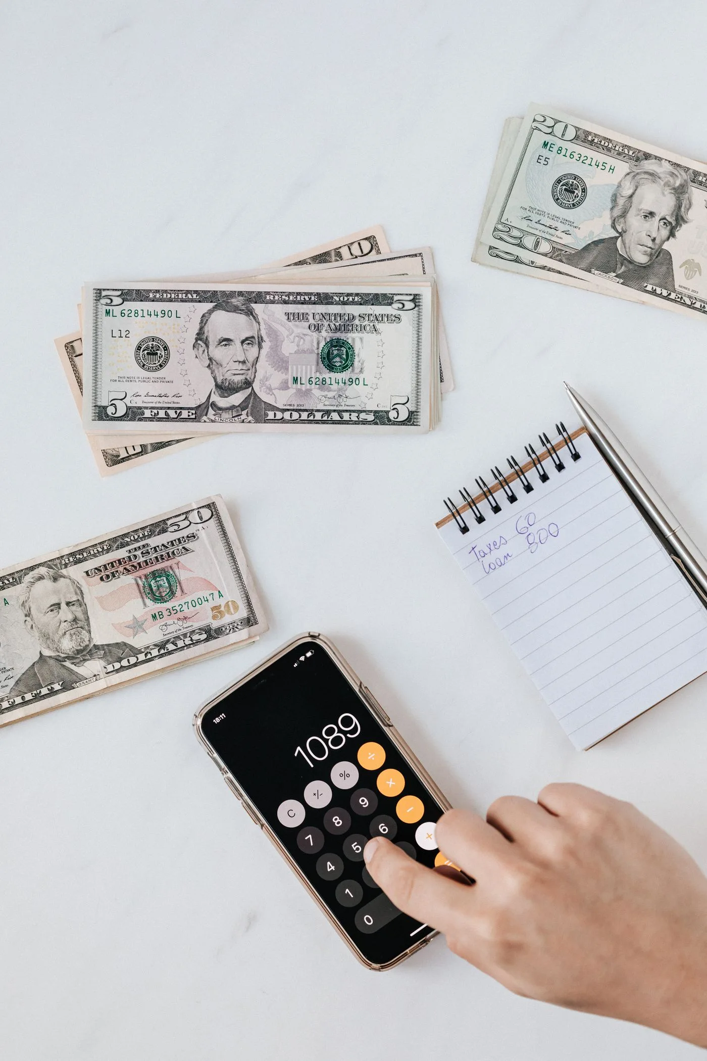 A person using a phone calculator beside dollar bills and a notebook