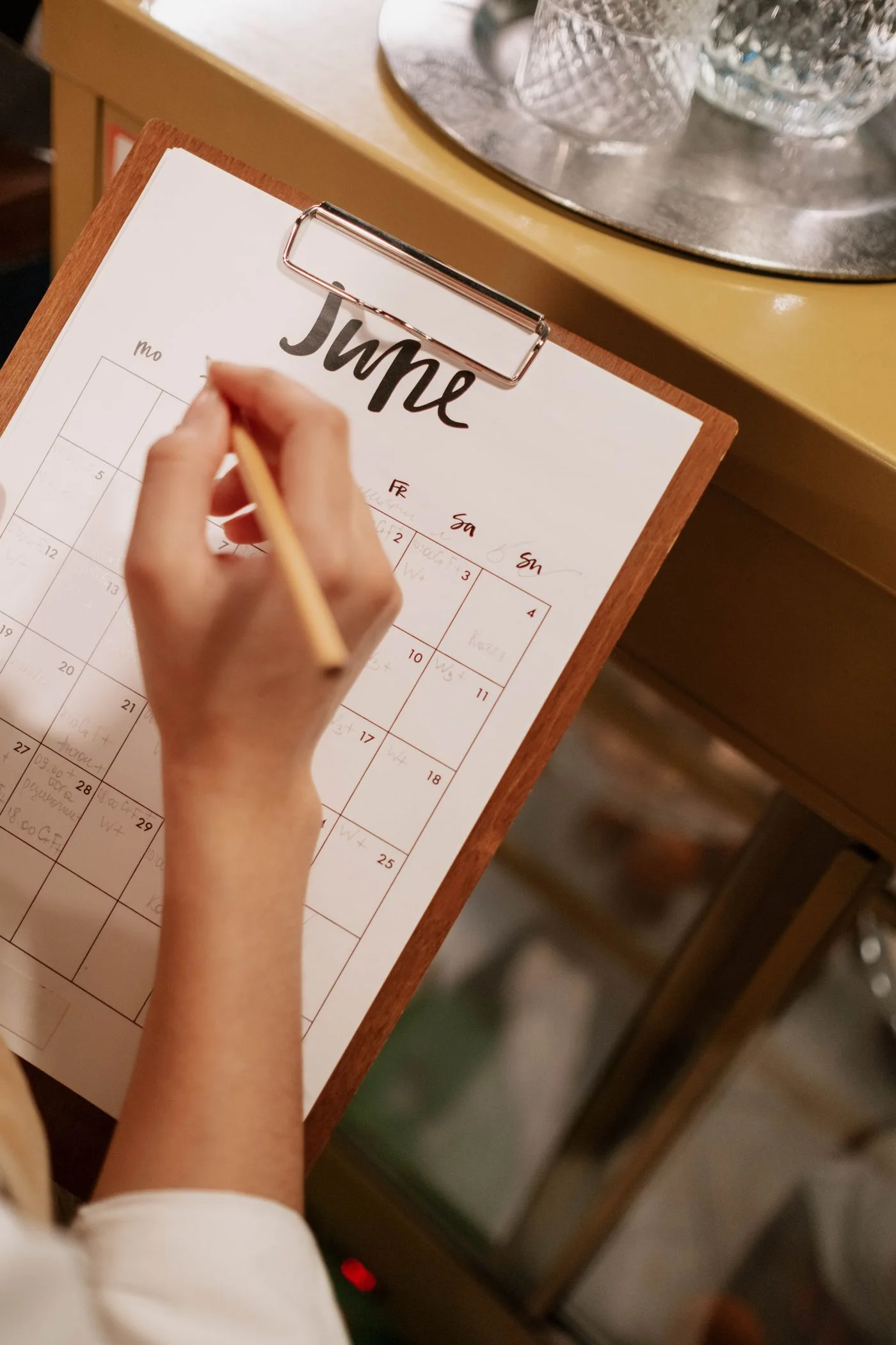Close-up of a hand writing on a June calendar using a pencil on a clipboard.